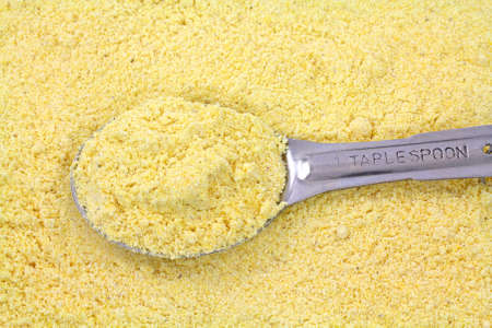 A filled tablespoon atop a layer of stone ground yellow corn meal.の写真素材