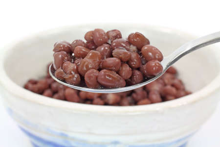 Spoon filled with azuki organic beans with a bowl and serving in the background.