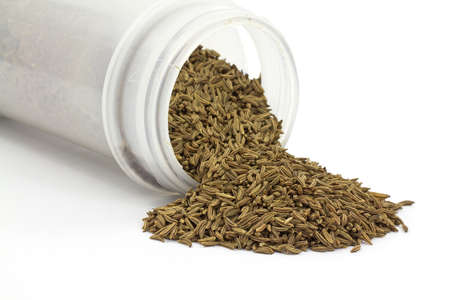 A small jar of caraway seeds on it's side with the seasoning spilling out.