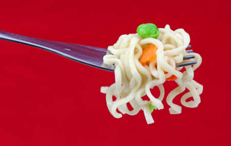 A fork with noodles peas and carrots on a red background.