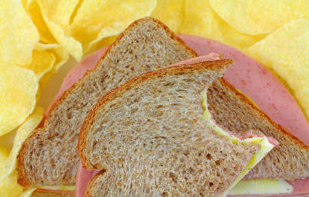 Close view of a bologna and cheese sandwich that has been cut in half and bitten on wheat bread with...