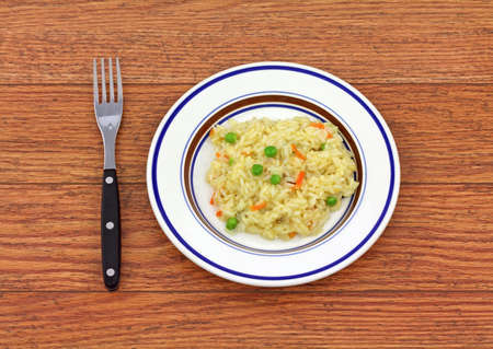 Small serving of rice pilaf in a dish with fork on a wood tabletop.の写真素材