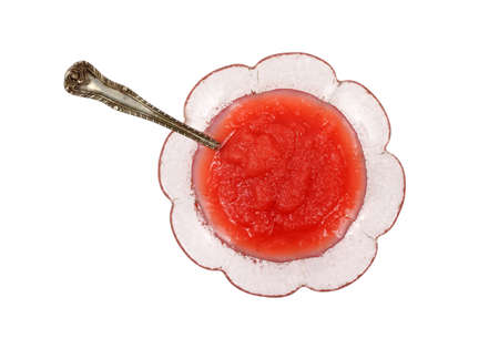 A small serving of strawberry applesauce in floral pattern dish with a spoon on a white background. 