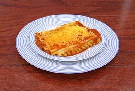 A small serving of lasagna on two blue plates atop a wood tabletop.の写真素材