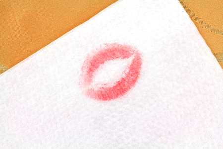 A white napkin with blotted red lipstick on a gold fabric cloth.