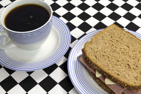 Cup of coffee with a turkey ham and cheese sandwich on a black and white checkerboard tablecloth. の写真素材