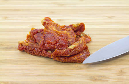 Close view of several sun dried tomatoes on a wood cutting board with pointed knife.の写真素材