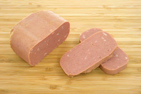 Close view of canned meat with two slices on a wood cutting board. の写真素材