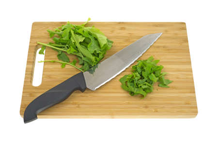 Several arugula leaves on a wood cutting board with knife.の写真素材