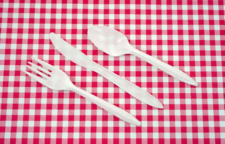 A set of plastic silverware arranged on a red and white picnic tablecloth.