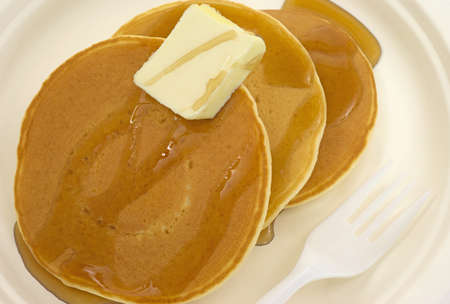 A close view of pancakes with butter and syrup on a paper plate with plastic fork 