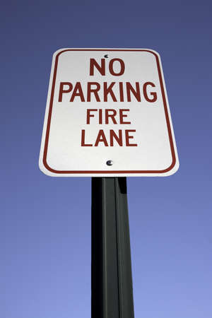 A bold No Parking Fire Lane sign on post against a blue sky の写真素材