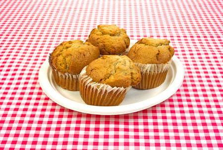 Four fresh apple spice muffins on a picnic plate set on a white and red checkerboard cloth の写真素材