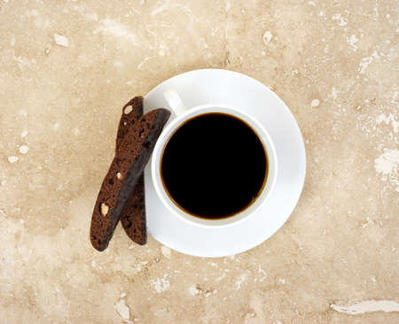 Top view of black coffee in white cup and saucer and chocolate biscotti on marble tabletop の写真素材