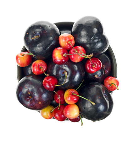 Top view of a bowl filled with ripe red cherries and plums on a white background の写真素材
