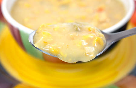 A spoonful of corn chowder in the foreground with the remainder of the meal in a bowl on a dish in the background の写真素材