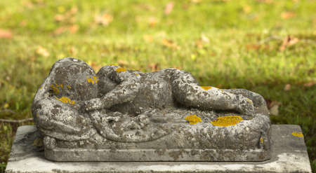 A very old headstone in the shape of a sleeping infant with lichen and moss の写真素材
