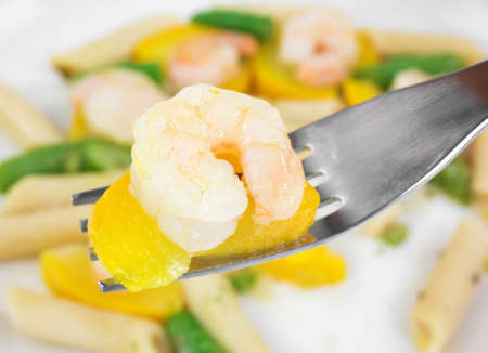 A fork with zucchini and a single shrimp in the foreground with the remainder of the meal in the background.の写真素材