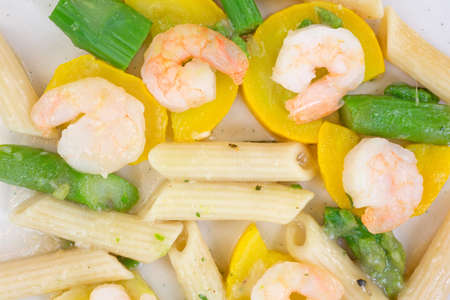 A close view of cooked shrimp, asparagus, zucchini and penne pasta on a plate の写真素材