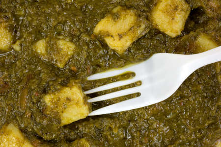 A very close view of pureed spinach with potato chunks and a white plastic fork.
