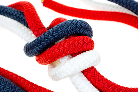 A very close view of  red white and blue rope in a tight knot on a white background.