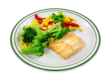 A small piece of haddock with broccoli, red peppers and corn on a green striped plate.の写真素材