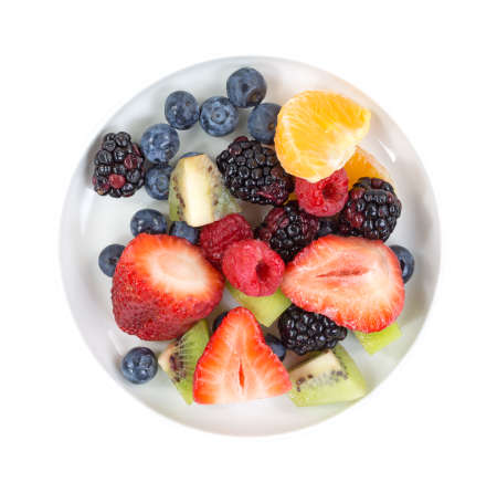 Top view of a small bowl with blueberries, red and black raspberries, kiwi, cut strawberries and an...