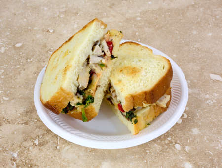 A toasted chicken sandwich on a small plate atop a marble countertop 