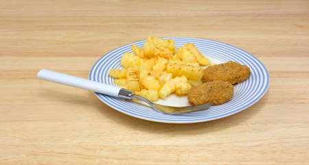 A plate of chicken nuggets with french fries and fork on a dining table の写真素材