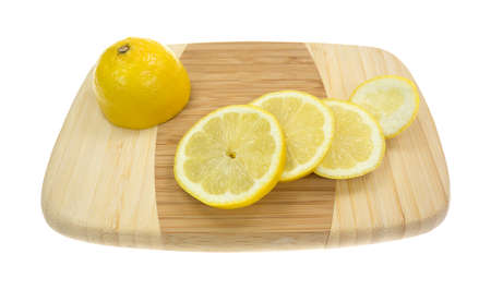 Half a lemon with several slices on a small bamboo cutting board の写真素材