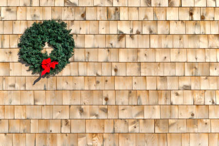 A small holiday Christmas wreath on a cedar shingle wall with a red ribbon の写真素材
