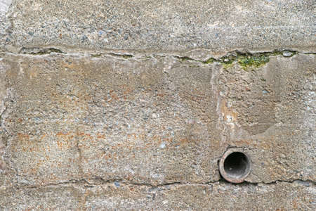 An old exterior retaining wall with a clay drainpipe and surface cracks with algae の写真素材