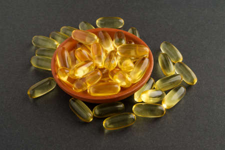 A small dish of cod liver oil capsules with several scattered atop a dark background 