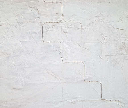 A stucco covered concrete block wall painted a light blue with cracks in the masonry.の写真素材