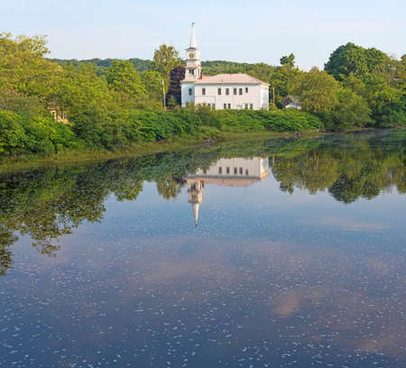 View of a white clapboard church with spire in the distance and a flowing river in the foreground in New England の写真素材