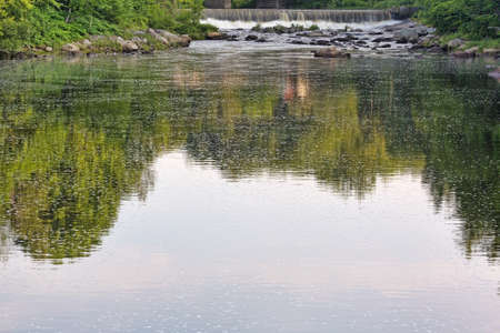 The distant falls in Frankfort Maine with the reflection of trees on the water.の写真素材