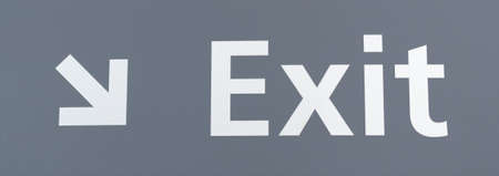 A white lettering exit sign with an arrow at an angle on a gray background.の写真素材