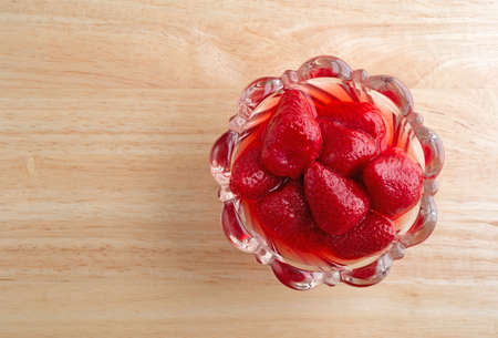 Top view of a glass bowl filled with canned strawberries in juice upon a wood table top.の写真素材