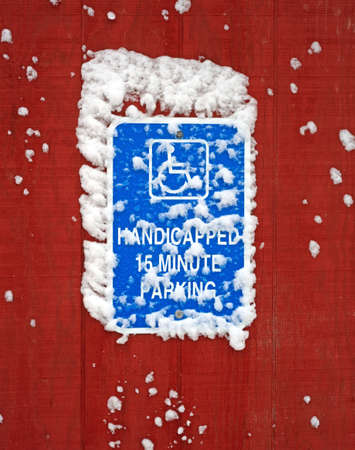 A bright blue handicapped parking sign with snow on sign and siding.の写真素材