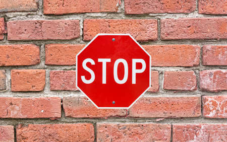A bright red and white stop sign securely attached to a large old brick exterior wall.の写真素材