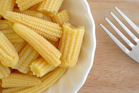 A very close view of small baby corn nuggets in a small bowl with a fork to the side on a wood table top.の写真素材