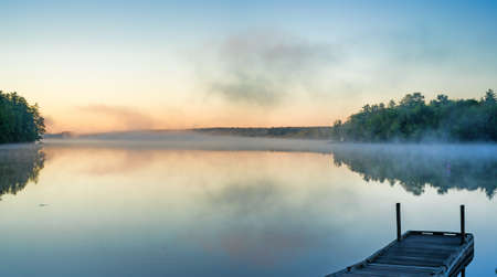 Toddy Pond, Maine, in the early morning light with reflected mist above the water and a small boat dock in the foreground.の写真素材