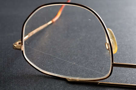 Close view of an old pair of eyeglasses with a scratched plastic lens on a dark background.の写真素材