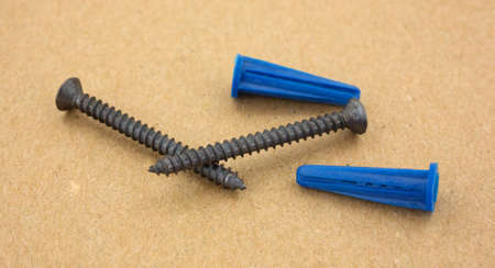 Two screws and blue wall anchors for hanging light objects on a cardboard background.
