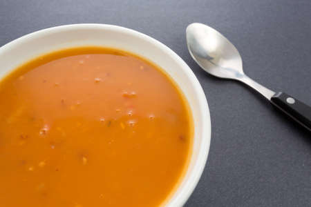 Close view of a bowl of tomato bisque soup with shrimp and garlic and a spoon to the side on a dark background illuminated by window light.の写真素材