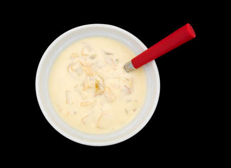 Top view of a serving of New England clam chowder in a bowl with a red handle spoon on a black background.の写真素材