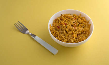 A serving of Mexican rice with a fork to the side on a yellow table illuminated with natural light...