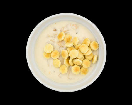 Top view of a serving of New England clam chowder in a bowl with oyster crackers on a black...