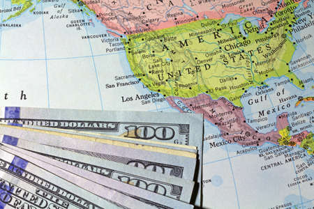 A partial view of hundred dollar bills atop an old atlas showing the United States and surrounding countries.の写真素材