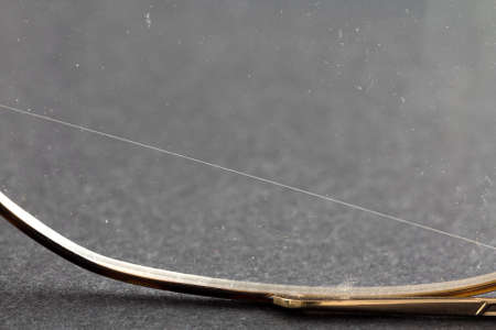 A very close view of an old pair of glasses with a sharp scratch across the lens.